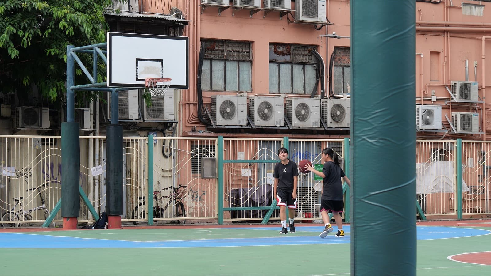 Two girls play basketball on a neighborhood court in Yuen Long, Hong Kong, on May 6, 2021 — the after-school hour that still needs lunch and a water bottle.