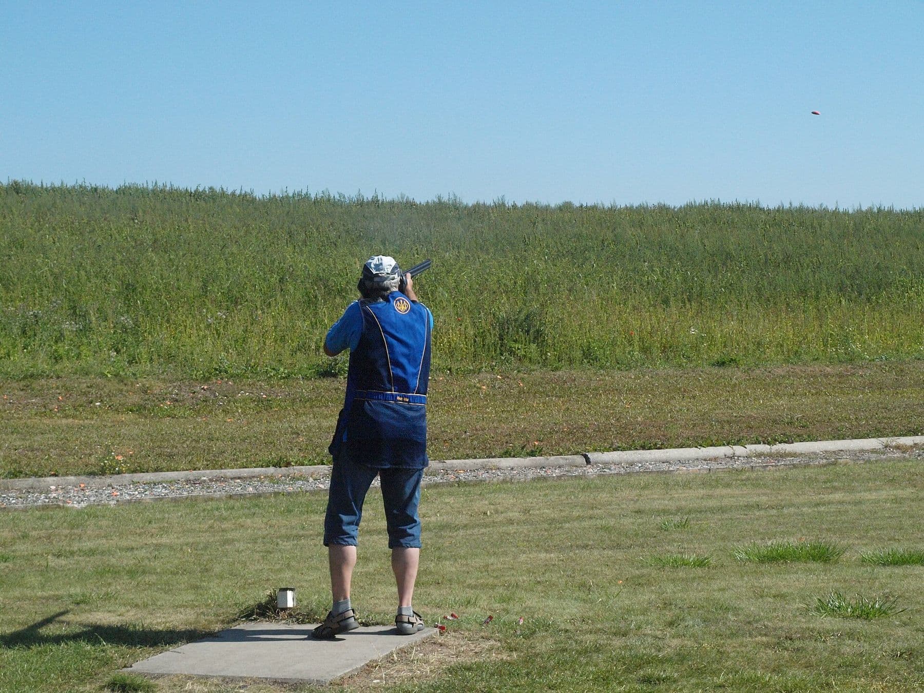 A trap shooter tracks a clay target on an outdoor range — the shotgun event Neeru Dhanda won in the rain at Aichi–Nagoya.